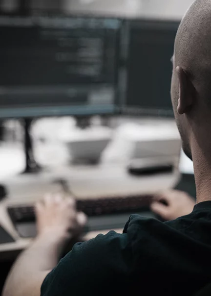 close-up shot over a man's shoulder who is coding at a desktop