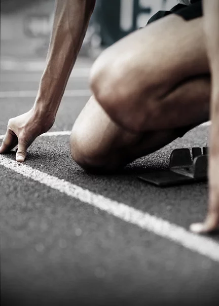 close-up on the starting line of a running track, showing the hands, lower arms and legs of a male runner kneeling in the starting block