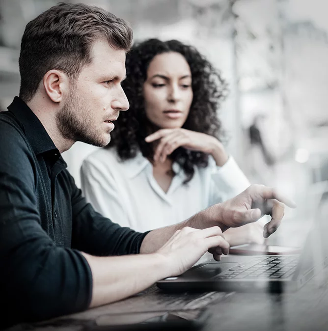 a man and a woman discuss a project while sitting in front of a Laptop