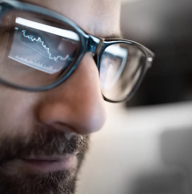 man with glasses that reflect his screen displaying a graph